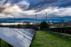 A landscape featuring rows of solar panels and tall wind turbines under a dramatic sky, representing green energy expansion.